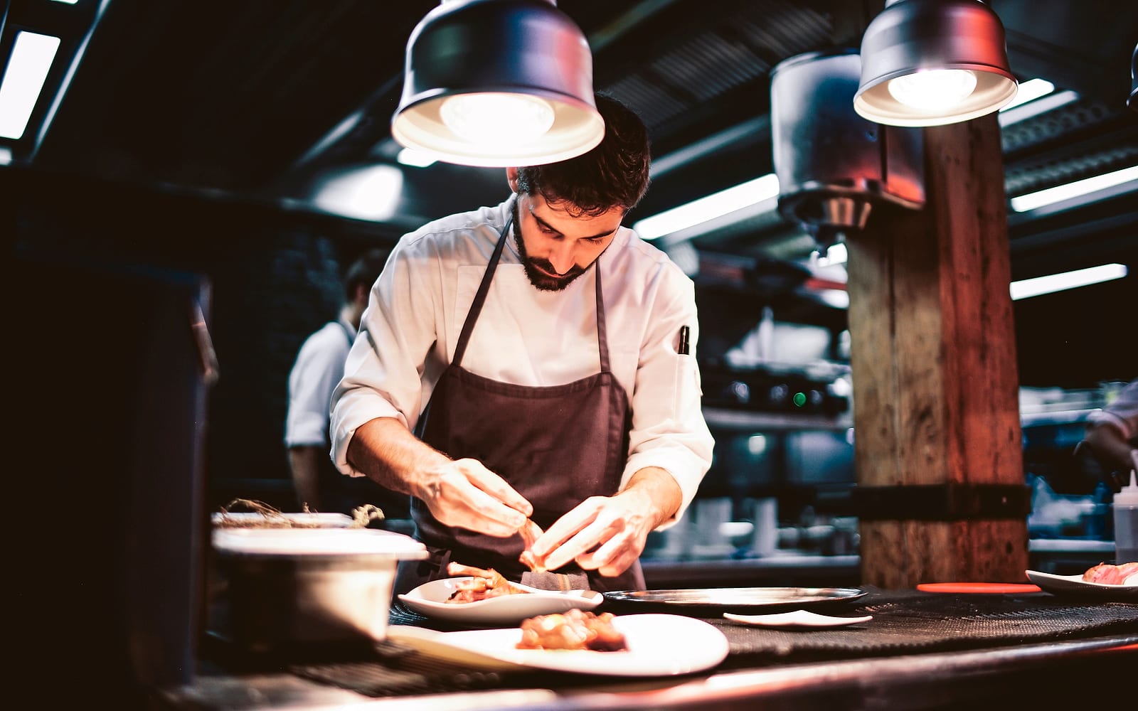 A chef plating dishes under the heat lamps on the pass