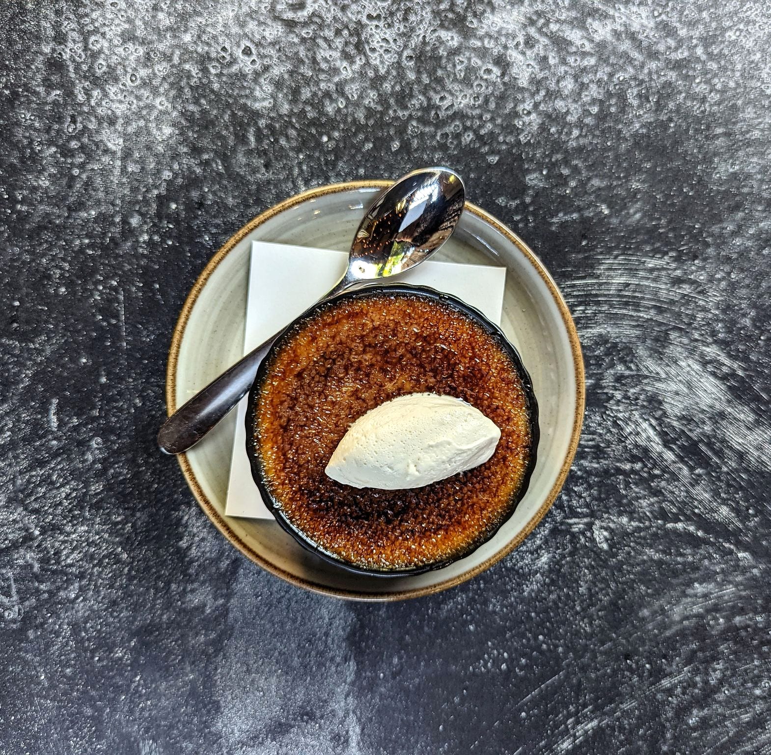 Crème brûlée topped with a quenelle of ice cream, a spoon on the side