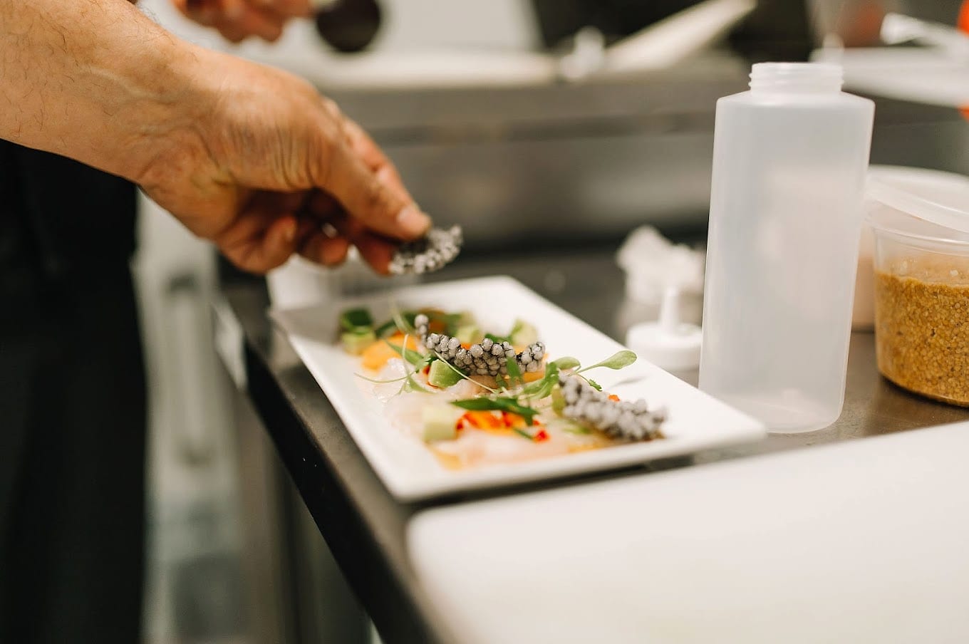A cook's hand garnishing a rectangular plate of crudo in Decant's kitchen