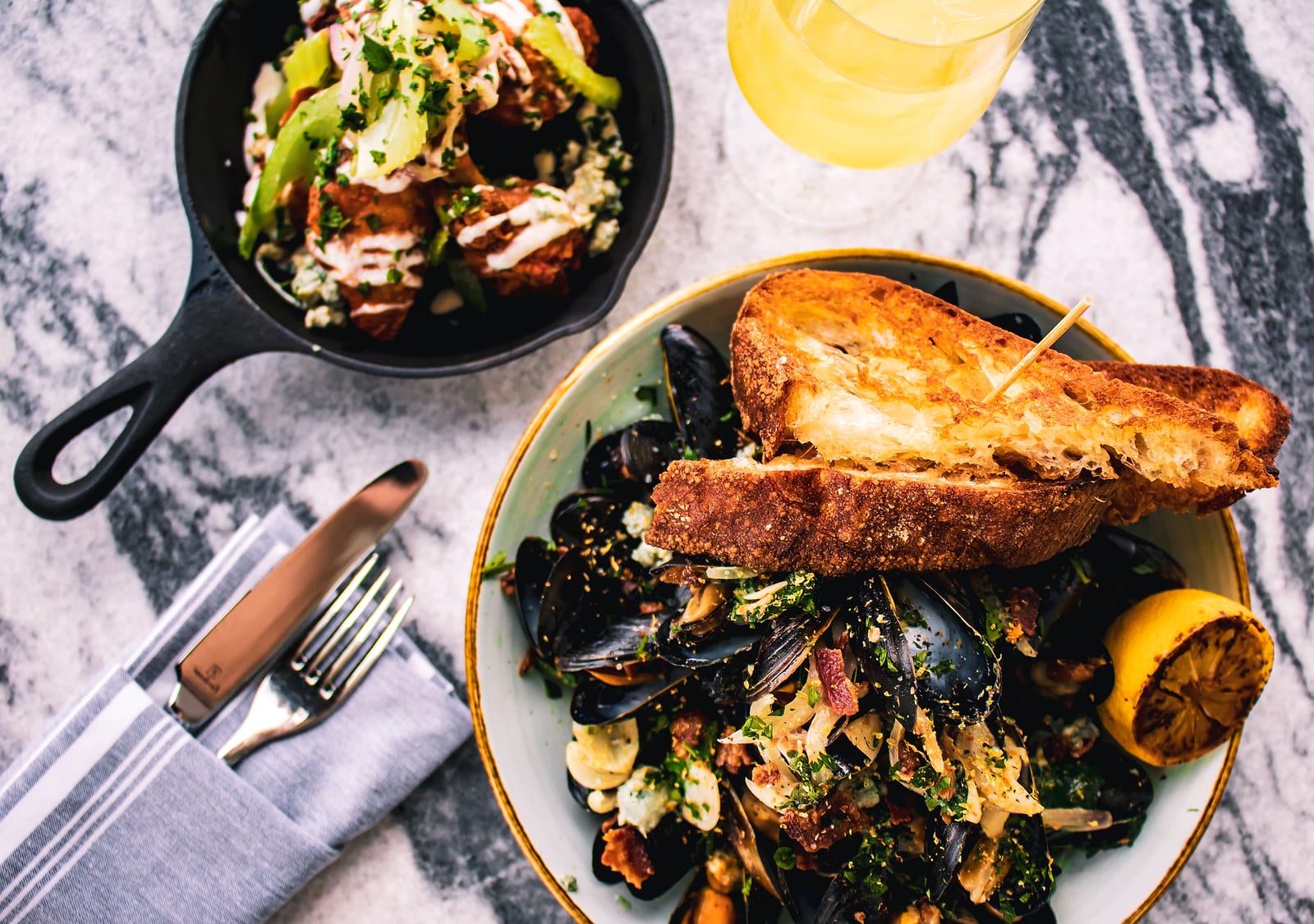 A bowl of mussels with grilled bread and charred lemon on a marble table