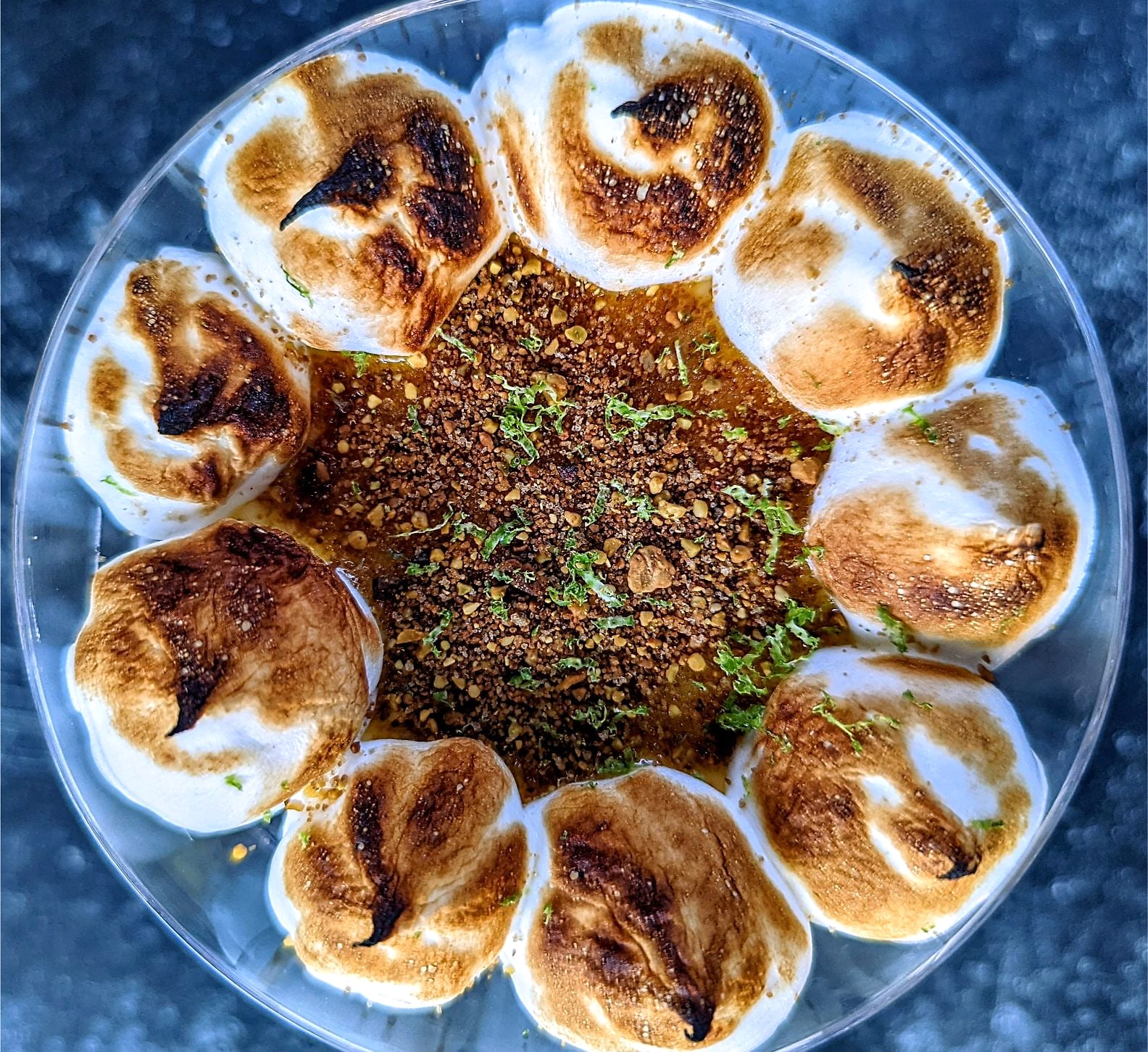 A dessert with torched meringue puffs around a crumb and citrus zest centre