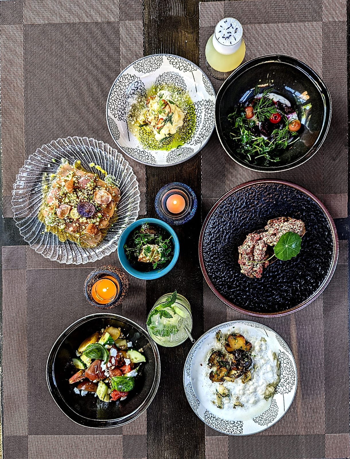 Overhead spread of small plates, salads and cocktails on a wooden table